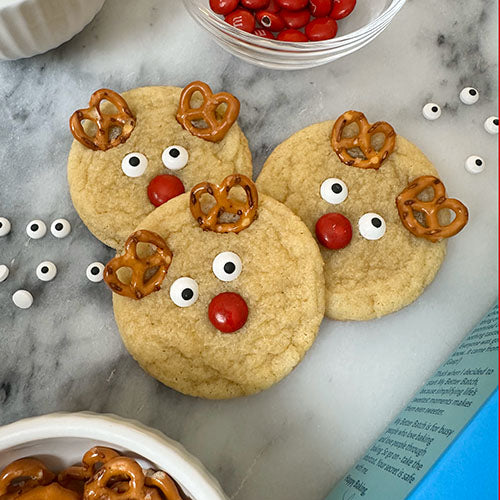 Three reindeer sugar cookies surrounded by decorations. 