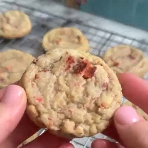 Strawberry sugar cookie held over a batch of freshly baked cookies. 